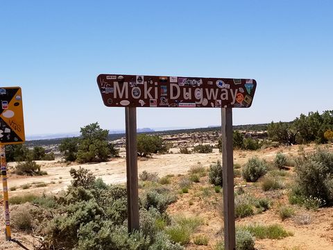 A brown road sign reading "Moki Dugway", plastered edge to edge with stickers, standing in desert scrub.
