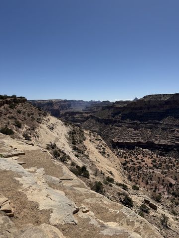 A slab-rock rim in the foreground dropping away into a wide canyon, with mesas and buttes strung along the far horizon.