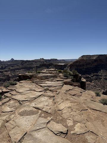 A flat pavement of cracked sandstone slabs running out to the edge of the rim, canyon and distant buttes beyond.