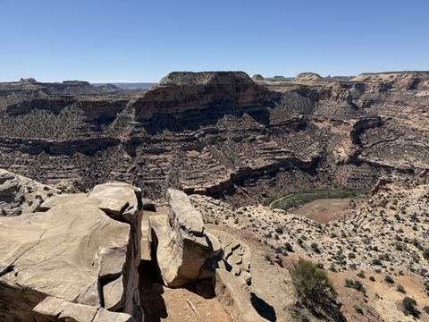 A split sandstone block on the rim, and past it a wide bend of the canyon with a green riverbank at its bottom.