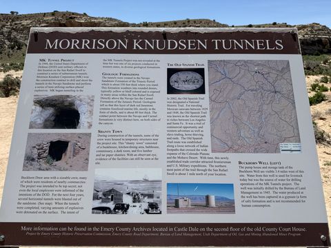 A large brown interpretive sign headed "Morrison Knudsen Tunnels," with historical photographs and panels on the tunnel project, local geology, and a nearby well.