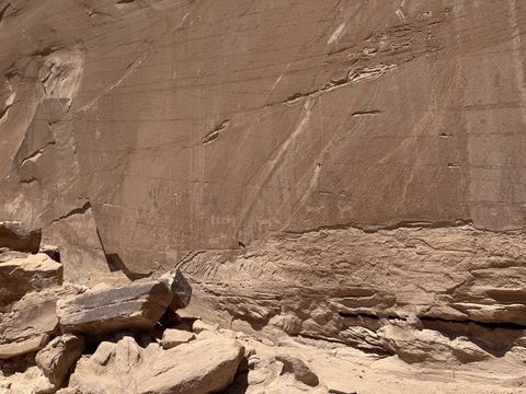 A tall, smooth sandstone wall streaked with desert varnish, faint markings across its lower face and a rubble ledge at its base.