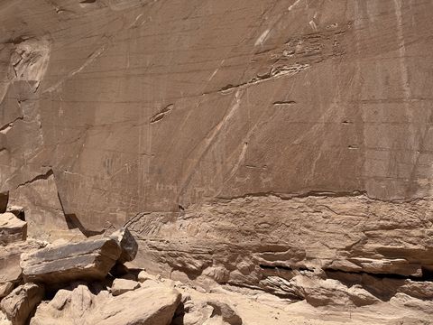 A closer view along the same varnished wall, faint pecked figures showing near the ledge line.