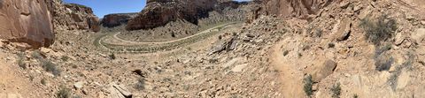 A wide panorama of the canyon, the dirt road switching back along the wash floor between the enclosing walls.