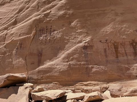 A wide section of the painted wall, with clusters of tall figures on the left and right and a jointed ledge of rock below.