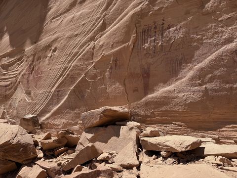 The pictograph panel viewed across a rubble slope, the painted figures a faint red cluster high on the sandstone.