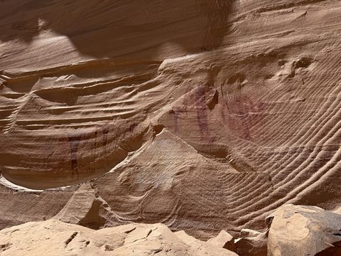 Faded red pigment on a swirling, cross-bedded sandstone wall, the paintings nearly lost in the rock's banding.