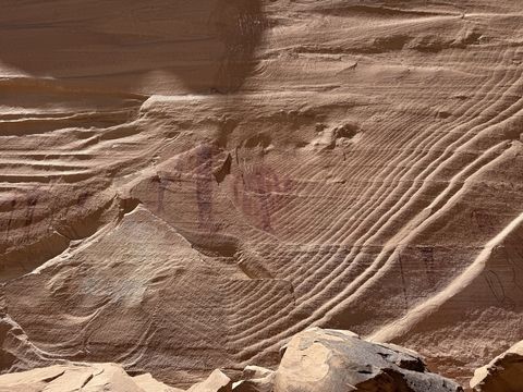Weathered painted figures on a cross-bedded wall in raking light, partly obscured by the sandstone's curving layers.