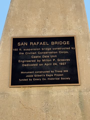 A bronze plaque on a concrete pillar reading that the San Rafael Bridge is a 160 ft suspension bridge built by the Civilian Conservation Corps and dedicated April 24, 1937.