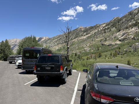 A trailhead parking lot with the Jeep, a van, and a sedan lined up in marked stalls below the rocky canyon headwall.
