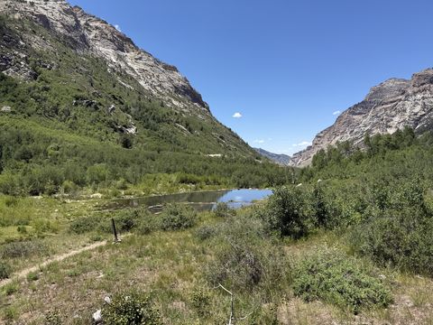 A small blue lake on the canyon floor, ringed by willow and aspen, with steep rock walls closing in on both sides.