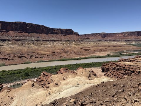 The Green River running along the base of a long banded cliff, seen across a bench of pale slickrock.