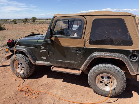 The Jeep parked on red dirt with an orange air hose running to a front tire, airing back up after the trail.
