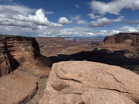 A flat slab of red sandstone at the rim, with Shafer Canyon opening out below and mesas ranked to the horizon.
