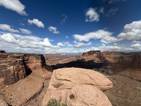 A broad slickrock ledge at the canyon rim, the canyon and its side drainages spread out beyond under a bright cloudy sky.
