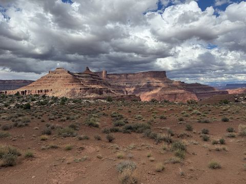 A desert flat of sparse grass below a long red mesa, dark storm clouds massing above it.
