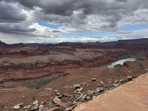 The Colorado River seen from the White Rim bench, its muddy channel curving between pale rock terraces under a broken sky.