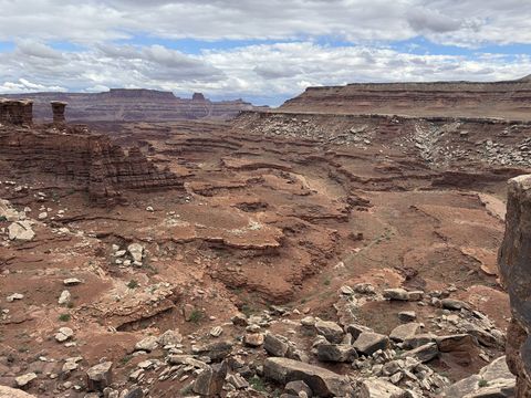 Broken red ledges and boulders below the White Rim, mesas and a distant butte on the skyline.