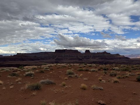A long banded mesa rising from a sagebrush flat, its rim broken into small towers, under a mottled sky.