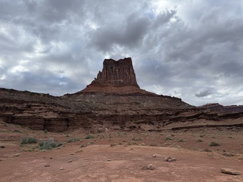 Airport Tower rising from a broad talus pedestal above the desert flat, dark clouds behind it.