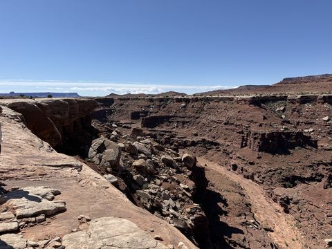 A deep, narrow slot cut into the rim, its rubble-filled bottom in shadow, open desert beyond.