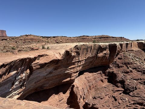 A cross-bedded sandstone wall curving along the rim of a small canyon, its swirling layers exposed in the sun.