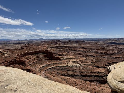 A wide, shallow basin of eroded red benches below the rim, mesas and mountains faint on the far horizon.