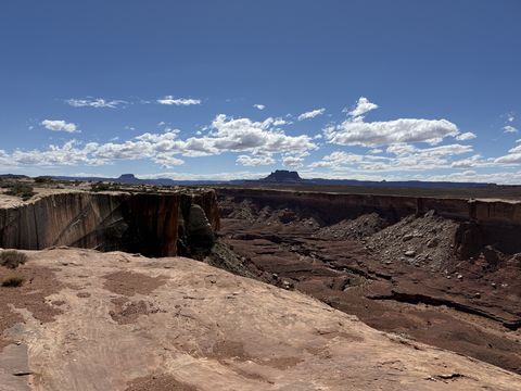 A slickrock rim in the foreground above a shadowed canyon, with a solitary butte standing on the distant horizon.