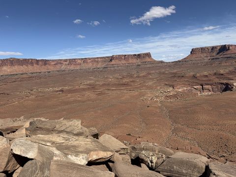 A broad desert bench below two flat-topped mesas, with a rubble of pale slabs in the foreground.