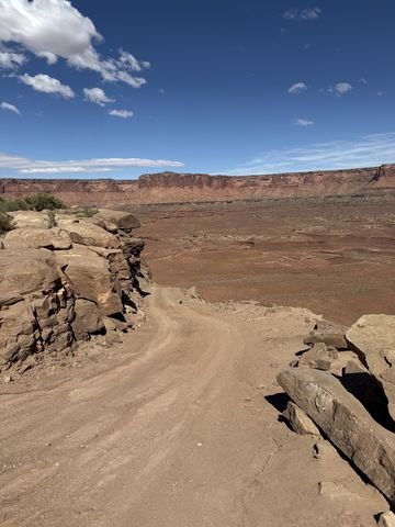 The White Rim road curving around a rocky point, dropping toward a broad flat with a long cliff line beyond.