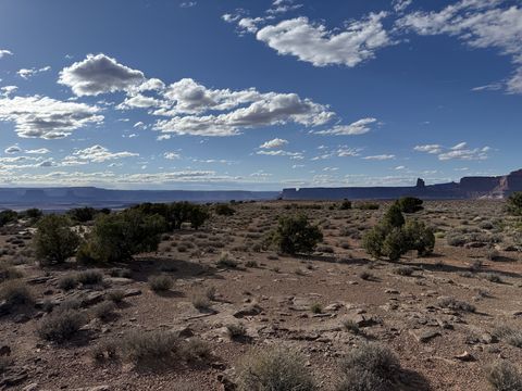 A sagebrush and juniper flat under scattered cumulus, with mesas and a distant tower along the skyline.