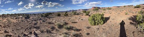 A wide panorama across a juniper-dotted bench to the mesas and cliffs on the horizon.