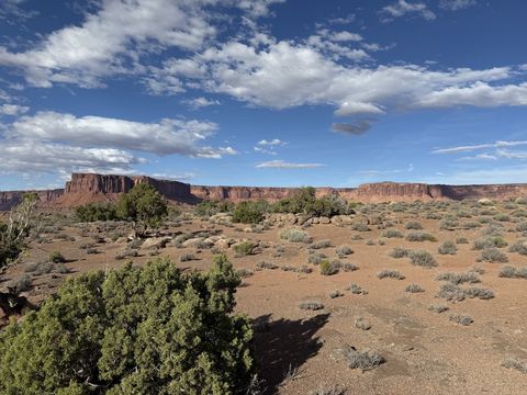 A long red mesa wall across a sagebrush flat, clouds building above it in late afternoon light.