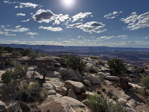 A rocky bench in backlit afternoon sun, the canyon and its far mesas hazy in the distance.