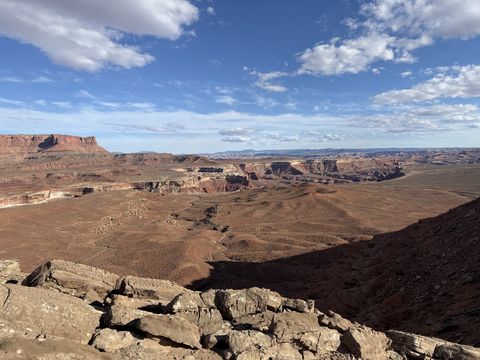 A broken rock rim in the foreground above a broad basin, a flat-topped mesa at the left and clouds overhead.