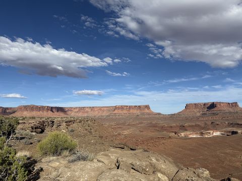 A line of red mesas across a bench of pale rock, afternoon clouds strung across the blue sky.