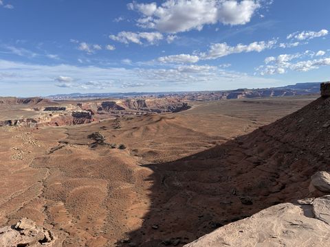 A dark rock spur in the foreground, with rolling red benches and distant mesas stretching away beyond it.