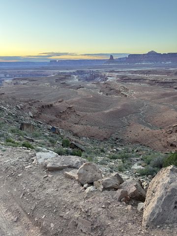 Dusk over the canyon from a high point, the sky fading to yellow behind silhouetted mesas, a rough road below.