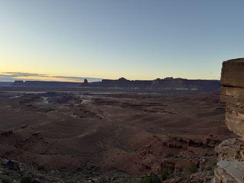 A wide basin at last light, buttes and mesas dark against a pale gold sky, a rock buttress at the right.