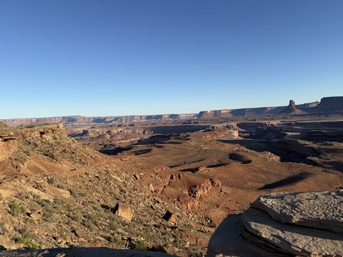 Long morning shadows across a red basin, with mesas and a spire on the sunlit skyline.