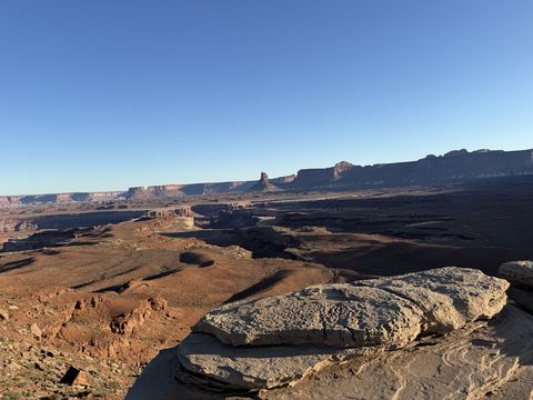 A slab of pale rock at the rim in morning light, the canyon and its far mesas spread out beyond.