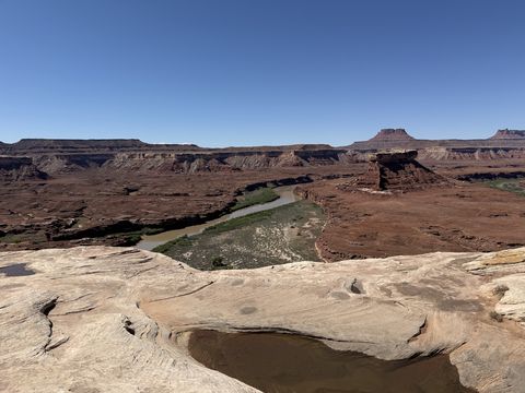 The Green River running green between its banks far below, a slickrock bench with a water-filled pothole in the foreground.