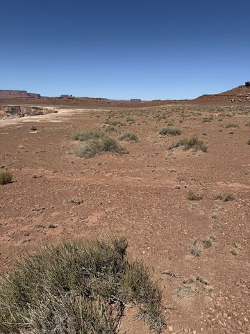 An open flat of red dirt and low brush under a cloudless sky, mesas low on the horizon.