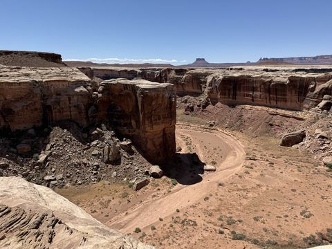 The road switchbacking through a gap between sheer red cliffs, with buttes visible on the skyline beyond.